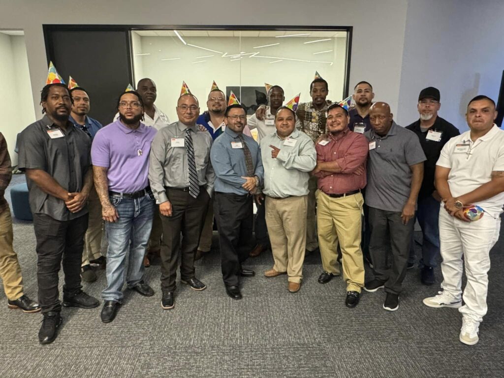 Group of PEP alumni wearing party hats and name tags gathered together indoors, smiling and celebrating an event.