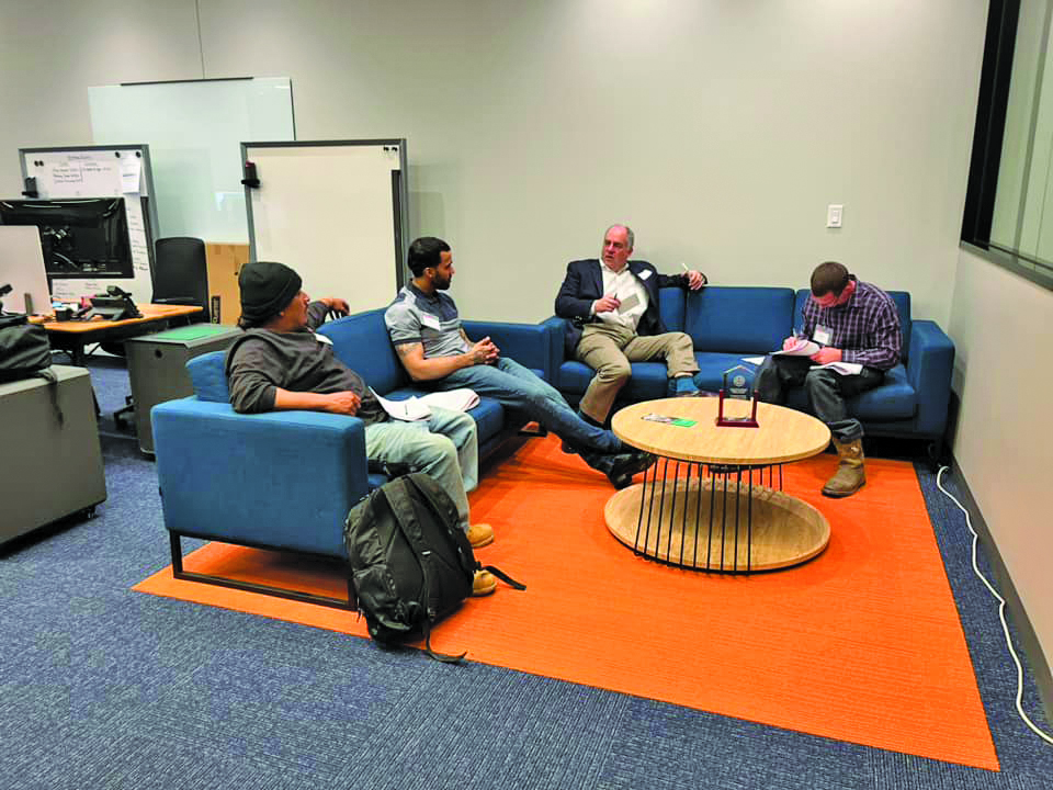 Small group of PEP participants and a mentor having a business discussion in a lounge area with notes and paperwork.