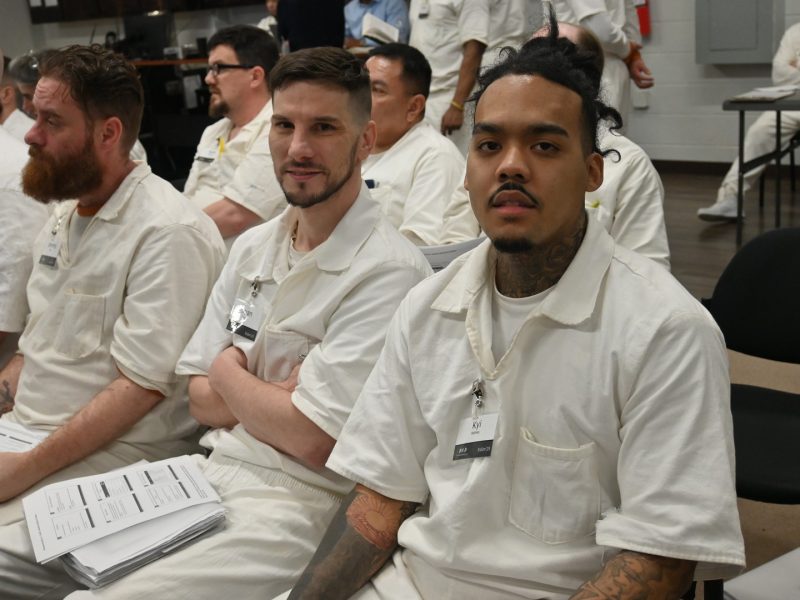 PEP participants in white uniforms sitting together in class, holding program materials during a session.