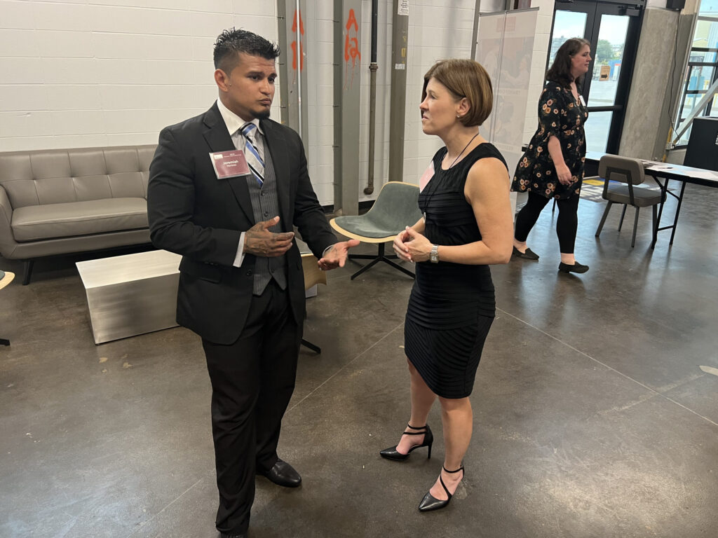 PEP participant in a suit speaking with a woman in a black dress during a professional networking or business event.