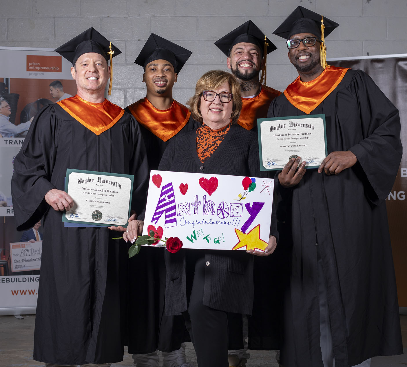 PEP graduates in caps and gowns celebrating with supporter holding congratulatory sign and diploma certificates