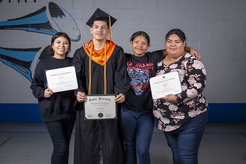ChatGPT said: PEP graduate in cap and gown proudly holding his diploma, standing with three supportive family members who are also holding certificates.