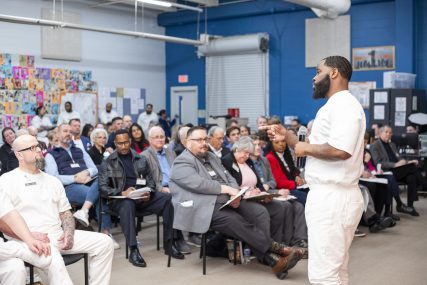 PEP participant presenting a business pitch with a microphone to a room of volunteers and executives.