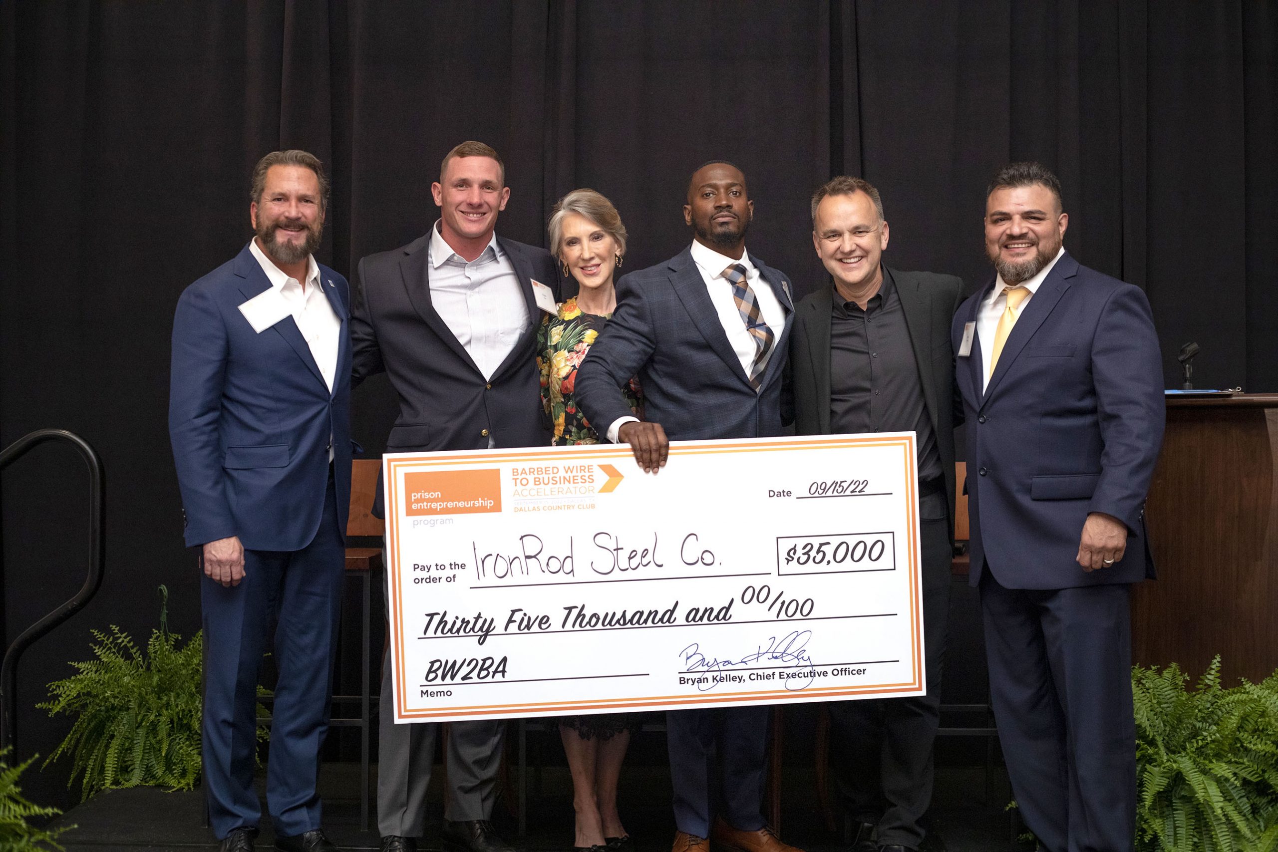 Group of six people in formal attire holding a large presentation check for $35,000 awarded to IronRod Steel Co. at a PEP Barbed Wire to Business Accelerator event.