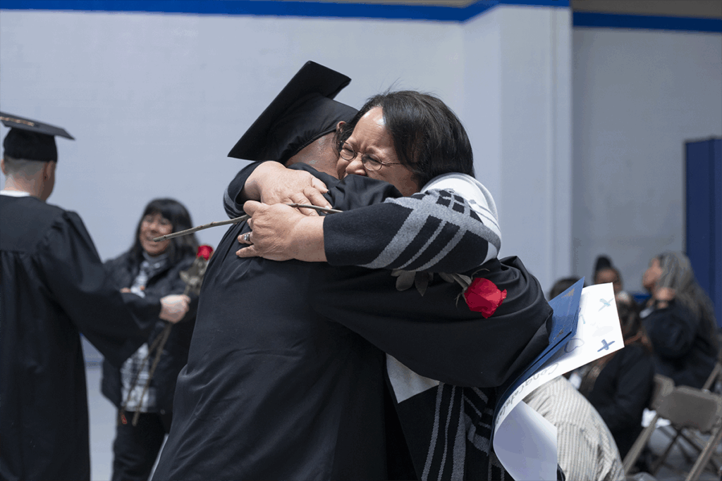 Graduate hugging a loved one while holding a rose during a PEP graduation ceremony